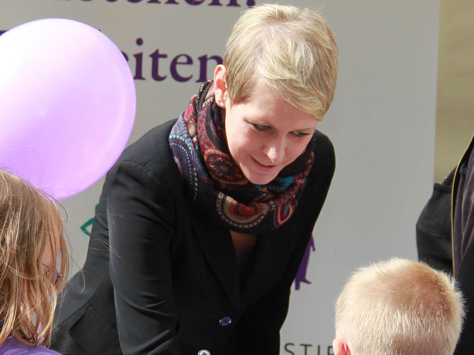 Eine Frau mit schwarzer Jacke posiert vor neutralem Hintergrund.