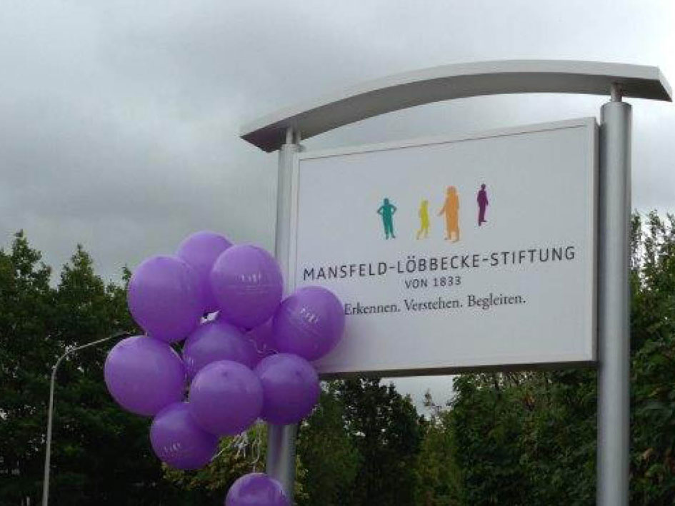 Vor einem Schild schweben lila Ballons, die die Aufmerksamkeit auf das Schild lenken.