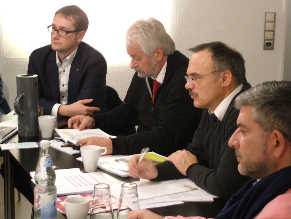 Eine Gruppe von Männern sitzt an einem Tisch mit Papieren und Stiften.