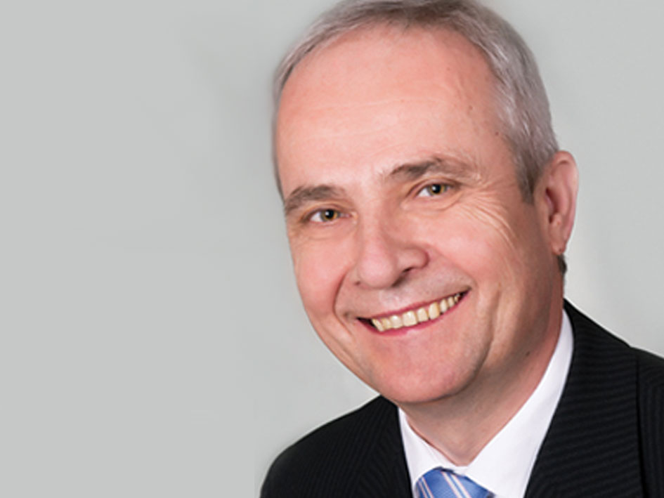 Ein Mann in Anzug und Krawatte lächelt freundlich in die Kamera.