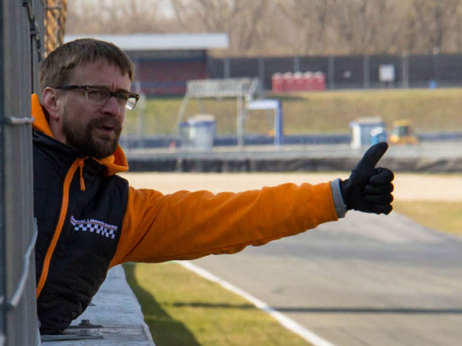 Ein Mann in einer orangefarbenen Jacke und schwarzen Brille zeigt mit dem Daumen nach oben.