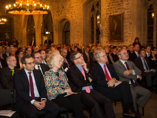 Eine Vielzahl von Menschen sitzt in einem Raum auf Stühlen und ist auf einen Vortrag konzentriert.
