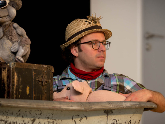 In einem Boot sitzt ein Mann mit Hut und Brille, umgeben von mehreren Stofftieren.