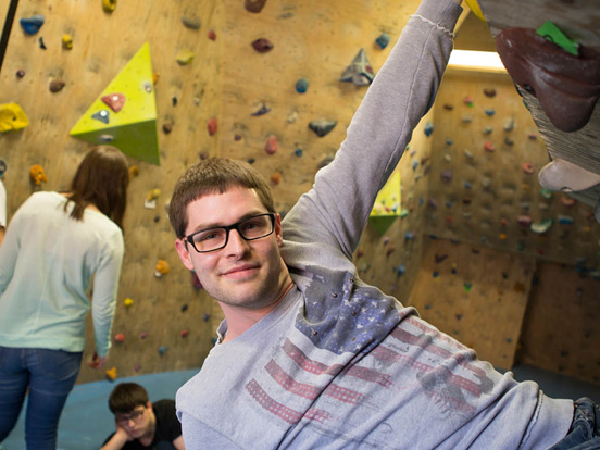 Ein Mann in Brille klettert an einer Wand und nutzt seine Kraft, um höher zu gelangen.