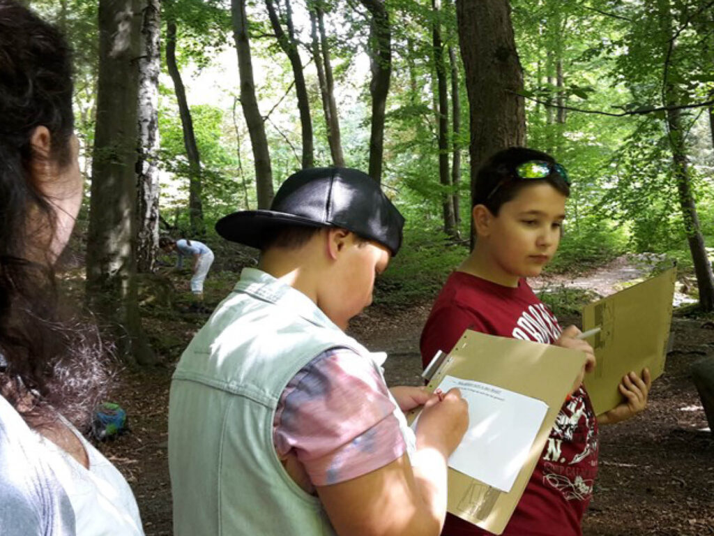 Drei Personen stehen im Wald und betrachten gemeinsam Dokumente.