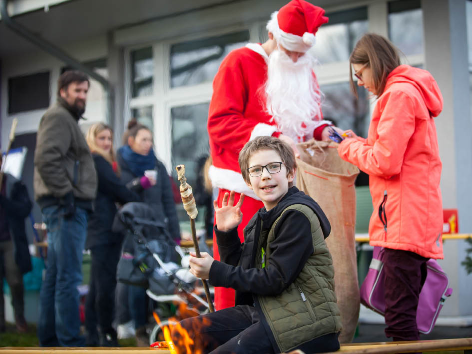 Weihnachtsmarkt: Kind grillt Stockbrot am Lagerfeuer, Nikolaus verteilt Geschenke. Winterliche Stimmung, Spaß für Kinder.