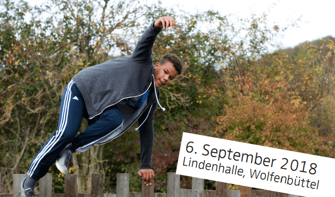 Parkour Athlet in Aktion: Junger Mann springt über Zaun, Sportliches Training im Freien, Lindenhalle Wolfenbüttel 6. September 2018.