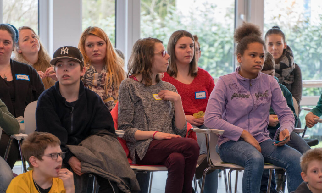 Gruppe junger Leute sitzt auf Stühlen bei einer Veranstaltung, Seminar oder Workshop. Junge Menschen, Zuhörer, Teilnehmer.
