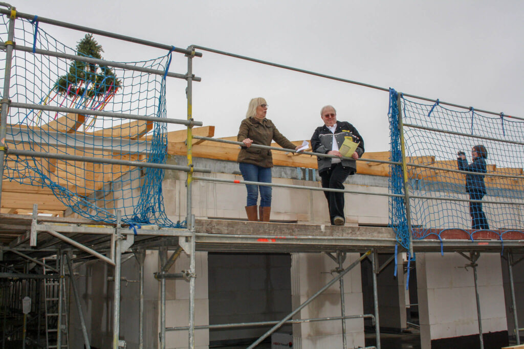 Richtfest: Bauarbeiter und Bauherren auf Gerüst am Rohbau mit Richtbaum. Neubau-Projekt, Hausbau mit Sicherheitsnetz.