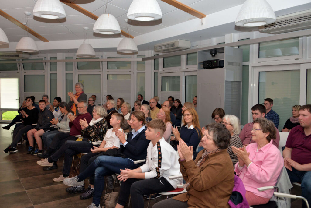 Publikum applaudiert bei einer Veranstaltung in einem hellen Raum. Menschen sitzen auf Stühlen und klatschen Beifall. Vortrag, Präsentation.