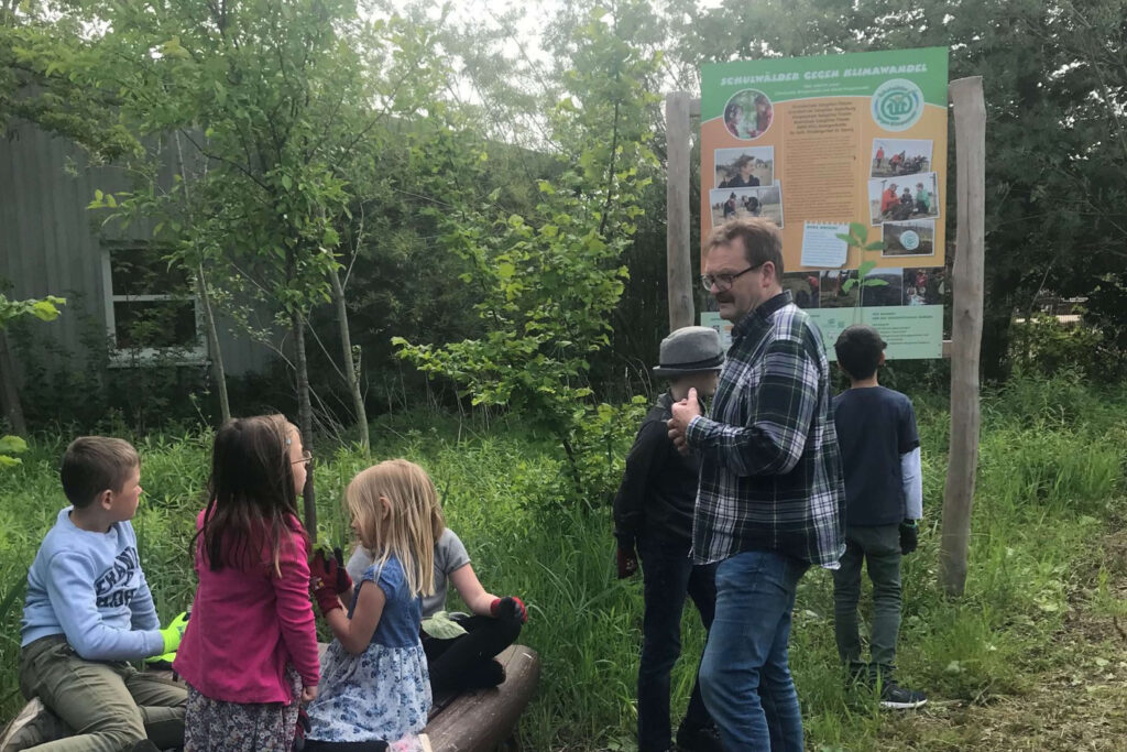 Schulwald gegen Klimawandel: Kinder lernen im Wald von einem Mann. Bildung für Nachhaltigkeit im Grünen. Natur erleben.