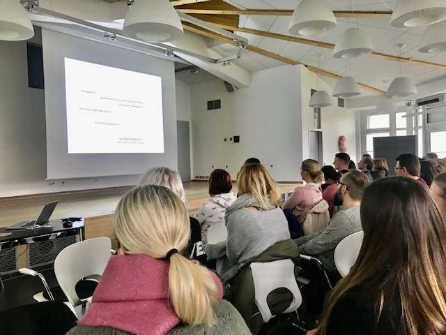 Publikum bei einer Präsentation/Vortrag in einem hellen Raum. Zuhörer schauen auf eine Leinwand mit Text. Konferenz, Seminar.
