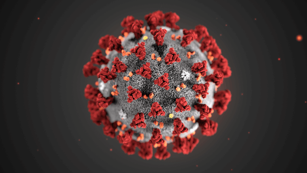 Ein digital gerendertes Bild eines Coronavirus zeigt ein kugelförmiges graues Viruspartikel mit roten Spike-Proteinen und kleinen gelben und weißen Punkten auf seiner Oberfläche vor einem dunklen Hintergrund.