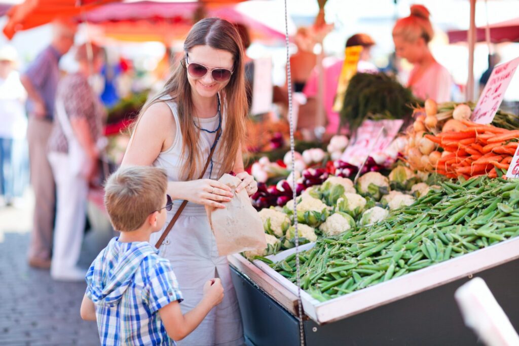 Mutter und Sohn kaufen frisches Gemüse wie Erbsen, Karotten und Blumenkohl auf dem Wochenmarkt.