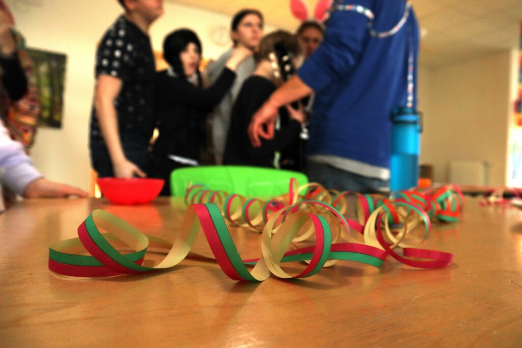 Partyhüte basteln: Luftschlangen auf Tisch, Gruppe von Leuten im Hintergrund, Fasching, Karneval, Geburtstag, Partydekoration, Feier.