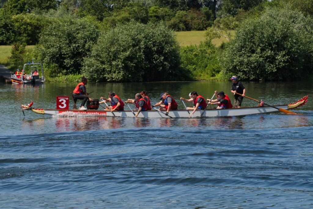 Drachenbootrennen: Team paddelt im Drachenboot mit der Nummer 3 auf dem Wasser, Wettkampf mit Paddelboot und Trommler.