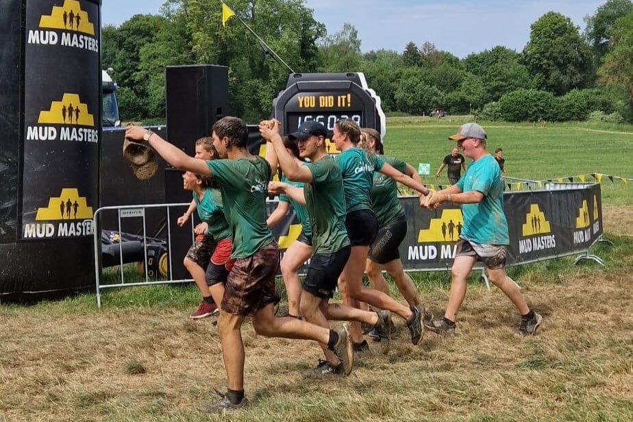 Mud Masters Team im Ziel: Schlammlauf-Teilnehmer feiern Erfolg beim Hindernislauf im Freien mit Zeitmessung.