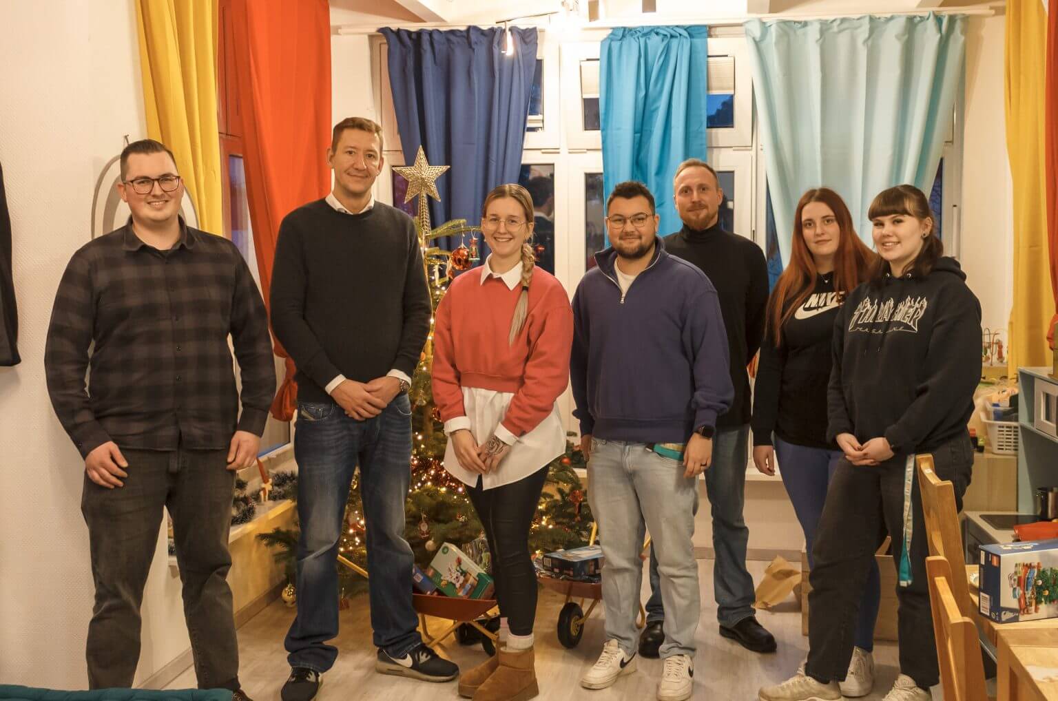 Gruppe junger Erwachsener posiert vor einem Weihnachtsbaum, festliche Stimmung, Teamfoto, Weihnachtsfeier, lächelnde Gesichter.