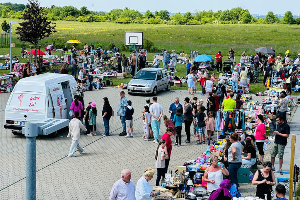 Eine große Gruppe von Menschen steht in einem Parkplatz und unterhält sich miteinander.