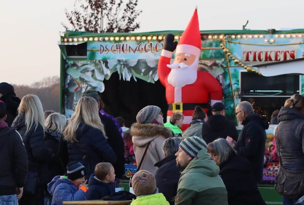 Eine Gruppe von Menschen feiert auf einem Weihnachtsmarkt mit dem Weihnachtsmann.