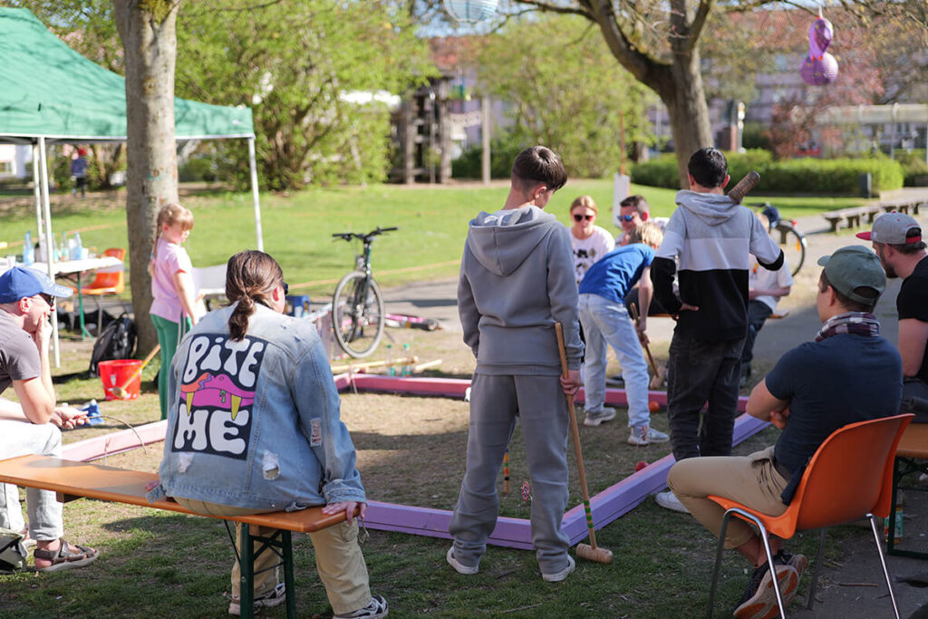 Krocket-Turnier im Park: Kinder und Erwachsene spielen Krocket im Freien, Freizeitaktivität, Familienspaß, Rasensport, Sommerfest, Outdoor-Spiel.