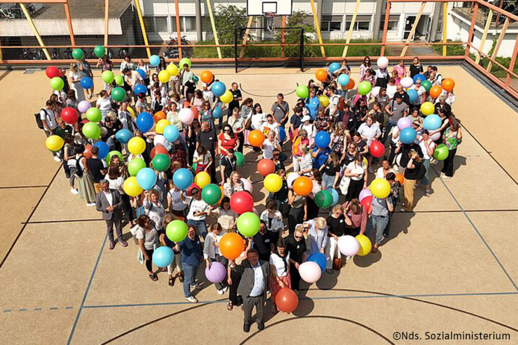 Menschen bilden mit Ballons in Herzform eine symbolische Darstellung von Liebe und Gemeinschaft.