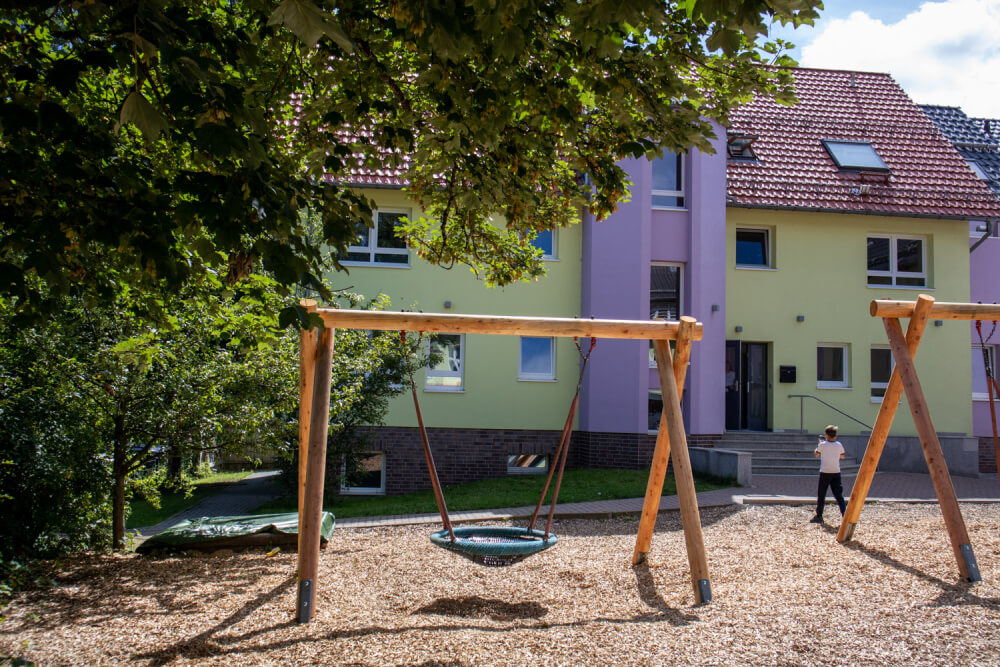 Spielplatz mit Schaukeln und einer Schaukelgruppe vor einem Gebäude.