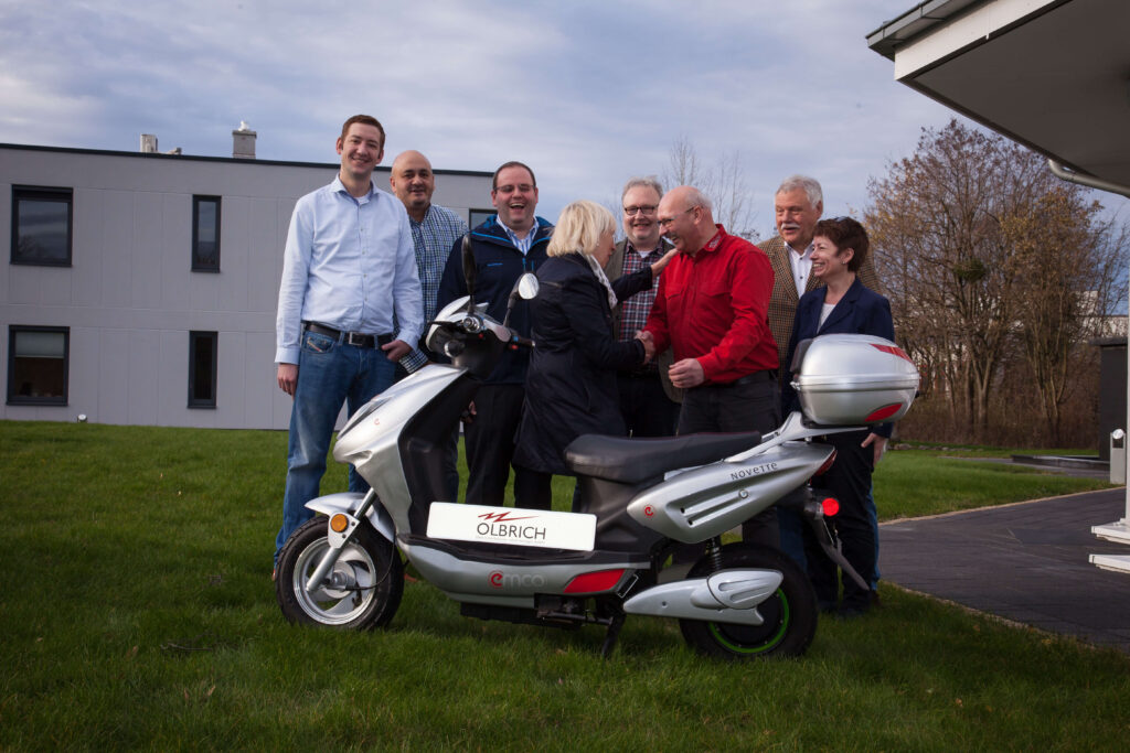 Fünf Personen stehen um einen Scooter herum und lachen in einer belebten Straße.