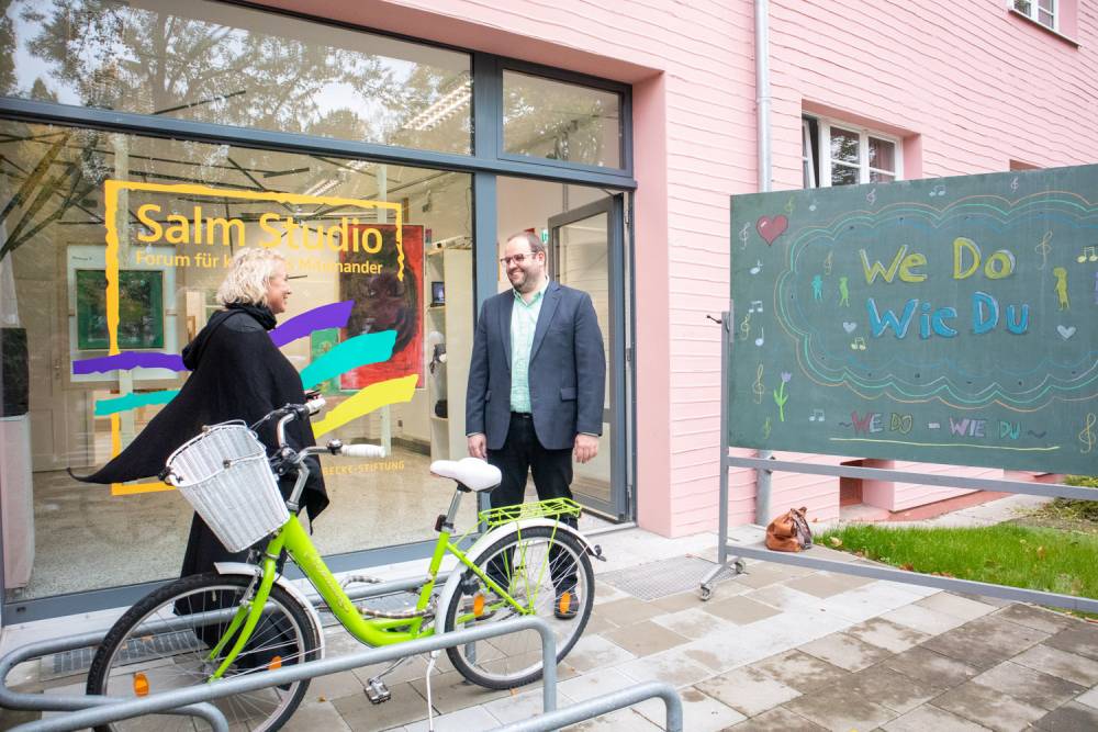 Zwei Menschen posieren vor einem Gebäude mit einem Fahrrad.