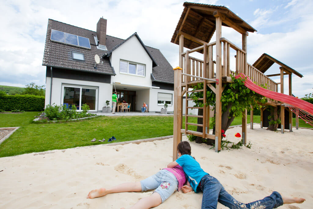 Zwei Kinder spielen fröhlich im Sand vor einem Haus.